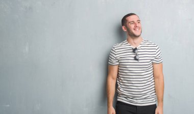 Gri grunge duvar uzak tarafına gülümseme ile yüzünde, doğal ifade seyir üzerinde beyaz delikanlı. Kendine güvenen gülüyor.