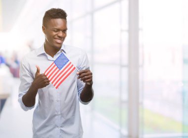 Ok işareti, başparmak ile parmak, mükemmel işareti yapıyor kocaman bir gülümseme ile ABD bayrağı mutlu tutan genç Afro-Amerikan adam