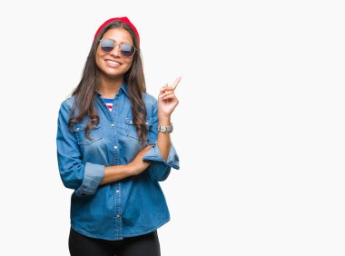 Kameraya bakarak yan el ve parmak ile işaret yüzünde kocaman bir gülümseme ile izole arka plan üzerinde güneş gözlüğü takmış genç güzel Arap kadın.