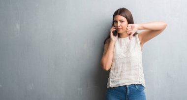 Kızgın yüz, eksi işareti aşağı antipati başparmak ile gösterilen, ret kavramı ile telefonda konuşurken grunge gri duvar genç esmer kadın