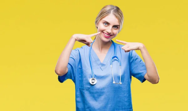 年轻美丽的金发医生外科医生护士妇女在孤立的背景微笑自信地显示和指着手指牙齿和嘴 健康理念 — 图库照片