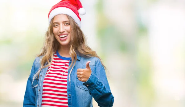 美丽的年轻金发女子戴着圣诞节帽子在孤立的背景做愉快的拇指手势与手 批准表达式看着相机显示成功 — 图库照片