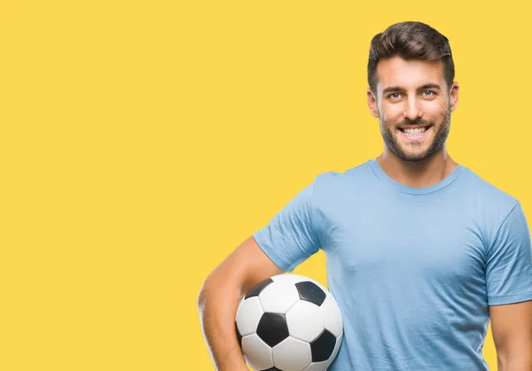 孤立した背景に立っていると自信を持って歯を見せて笑顔で笑っている幸せそうな顔でサッカー サッカー ボールを保持している若いハンサムな男 — ストック写真