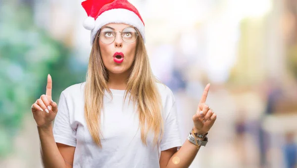 若い美しい女性隔離された背景にクリスマスの帽子をかぶってびっくり驚いて見上げると指で指していると腕を上げた — ストック写真
