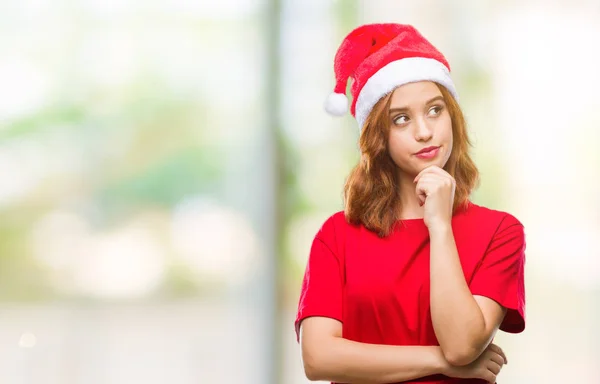 年轻美丽的女人在孤独的背景下戴着圣诞帽 手放在下巴上思考问题 沉思的表情 微笑与周到的脸 怀疑概念 — 图库照片