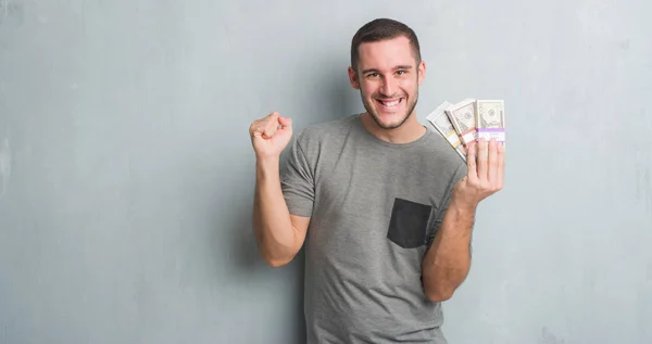 Young Caucasian Man Grey Grunge Wall Holding Bunch Money Screaming — Stock Photo, Image