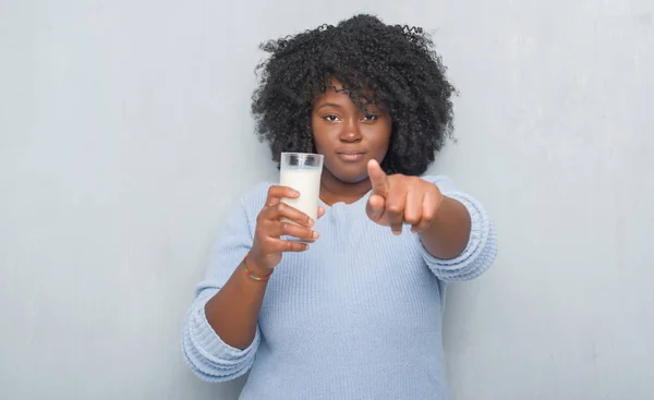 Young african american woman over grey grunge wall drinking a glass of milk pointing with finger to the camera and to you, hand sign, positive and confident gesture from the front