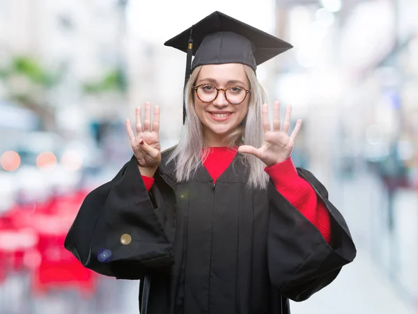 孤立した背景表示と指で上向きに大学院の制服を着て若いブロンドの女性ナンバー ナイン自信を持って 幸せな笑みを浮かべて — ストック写真