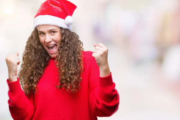 笑顔と成功のために叫んで 上クリスマスの帽子を着ている若いブルネットの少女は非常に幸せと興奮の腕を上げ 勝者のジェスチャを行う背景を分離しました お祝いのコンセプト — ストック写真