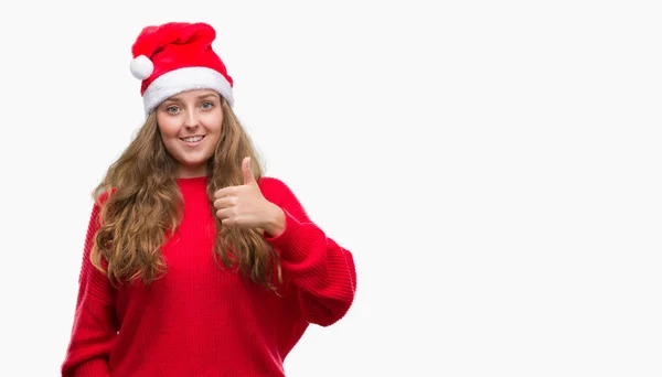 戴着圣诞老人帽子的年轻金发女郎高兴的笑着做 拇指与手指 优秀的标志 — 图库照片