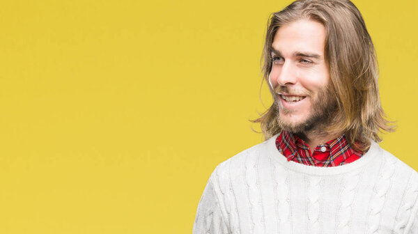 Young handsome man with long hair wearing winter sweater over isolated background looking away to side with smile on face, natural expression. Laughing confident.