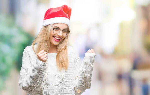 笑顔と成功のために叫んで 上クリスマスの帽子を着ている若い美しいブロンドの女性は非常に幸せと興奮の腕を上げ 勝者のジェスチャを行う背景を分離しました お祝いのコンセプト — ストック写真