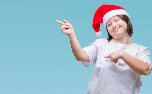 有唐氏综合症的年轻成年妇女戴着圣诞帽在与世隔绝的背景下微笑着 看着两只手和手指指向侧面的相机 — 图库照片