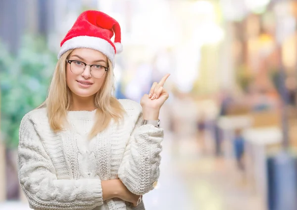 カメラを見ている側の手と指で指すの顔に大きな笑みを浮かべて隔離された背景にクリスマスの帽子をかぶって若い白人女性 — ストック写真
