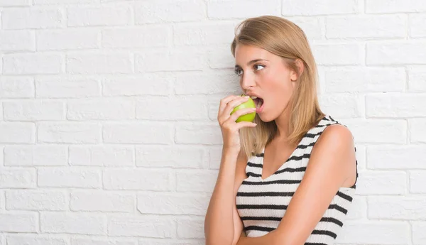 Hermosa Mujer Joven Sobre Pared Ladrillo Blanco Comiendo Manzana Verde — Foto de Stock