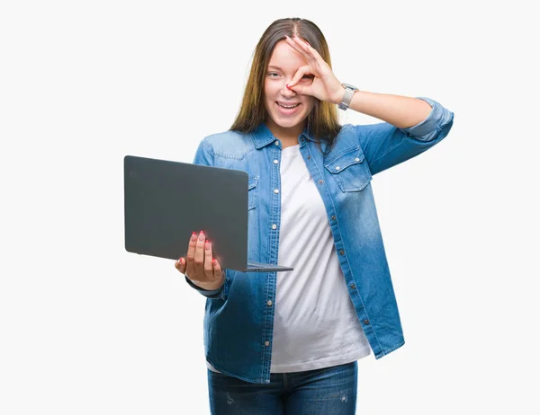 年轻的高加索妇女使用笔记本电脑在孤立的背景与快乐的脸微笑做确定的标志与手在眼睛上看着通过手指 — 图库照片