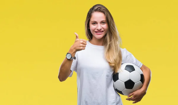 若い美しいブロンドの女性の上のサッカー ボールを保持している笑顔の サイン 優秀な兆候を親指をやって幸せなバック グラウンドを分離 — ストック写真