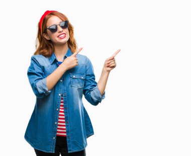 Gülümseyen ve iki elleri ve parmakları ile tarafına işaret kamera bakarak güneş gözlüğü takıyor izole arka plan üzerinde genç güzel kadın.