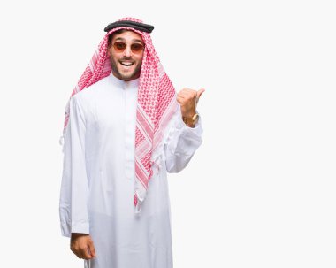 Keffiyeh seyir ve başparmak yanında yukarıyı mutlu yüz ile gülümseyen izole arka plan üzerinde giyen genç yakışıklı adam.