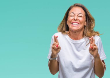 Orta yaş İspanyol kadın kıdemli geçiş parmakları umut ve gözleri kapalı ile gülümseyen izole arka plan üzerinde. Şans ve batıl kavramı.