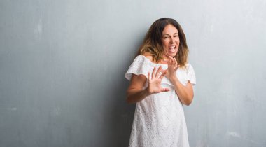 Orta yaş İspanyol kadın gri grunge duvardan ayakta tiksinti ifadesi, memnun ve korkulu tiksinti yüz yapıyorsun çünkü nefret tepki. Elleriyle kaldırdı. Sinir bozucu kavramı.