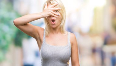 Yüz ve gözler el ile kapsayan şok bakmak izole arka plan üzerinde genç güzel sarışın kadın mahcup ifadeyle parmaklarımın arasından arıyorsunuz.