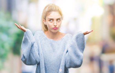 İzole arka plan clueless ve şaşkın bir ifadeyle kollar ve eller kaldırdı üzerinde kış kazak giyen genç güzel sarışın ve mavi gözlü kadın. Şüphe kavramı.