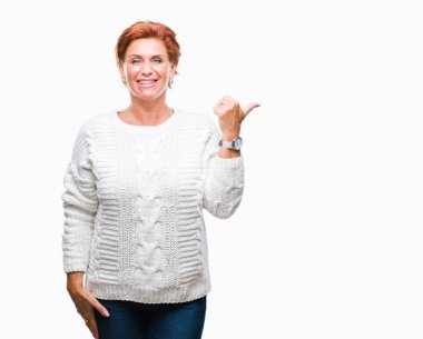 Seyir ve başparmak yanında yukarıyı mutlu yüz ile gülümseyen izole arka plan üzerinde kış kazak giyen Atrractive üst düzey beyaz Kızıl saçlı kadın.