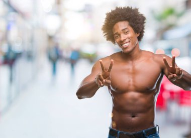 Çıplak vücut zafer işareti yapıyor parmak gösterilen kamera seyir gülümseyen izole arka plan üzerinde gösterilen Afro Amerikalı gömleksiz adam. İki numaralı.