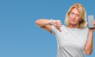 Orta yaş sarışın kadın gösteren boş ekran smartphone kızgın yüzü, eksi işareti aşağı antipati başparmak ile gösterilen, ret kavramı ile izole arka plan üzerinde