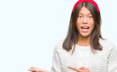 Hayret ve el ile sunulması ve parmak ile işaret ederken kameraya gülümseyen izole arka plan üzerinde kış kazak giyen genç Asyalı kadın.