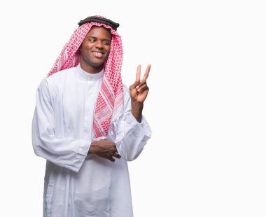 Mutlu yüz zafer işareti yaparken kameraya göz kırpıyor ile gülümseyen izole arka plan üzerinde geleneksel keffiyeh giyen genç Arapça Afrika adam. İki numaralı.