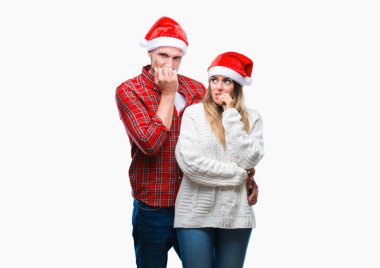 Genç çift aşık stresli ve gergin elle çivi ısırma ağzına bakarak izole arka plan üzerinde Noel şapka giyiyor. Anksiyete sorunu.