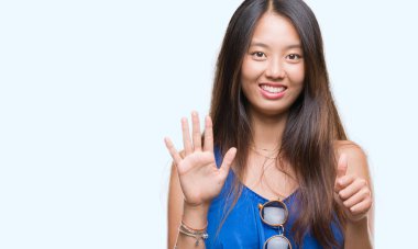 Genç Asyalı kadın gösterilen ve parmakları ile işaret izole arka plan üzerinde kendinden emin ve mutlu gülümseyerek süre 6 numara.