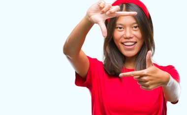 Genç Asyalı kadın elle yapma çerçeve ve parmakları ile mutlu yüz gülümseyen izole arka plan üzerinde. Yaratıcılık ve Fotoğrafçılık kavramı.