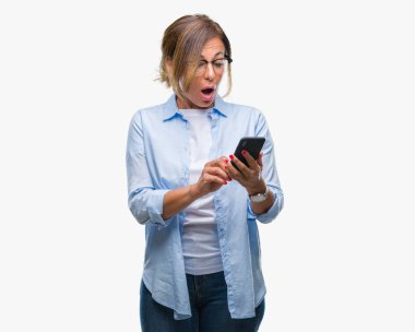 Orta yaş kadın kıdemli manifatura izole arka şok sürpriz yüzü, korkuyor ve korku ifadesi ile heyecanlı olan korkmuş üzerinden Smartphone kullanarak ileti gönderme