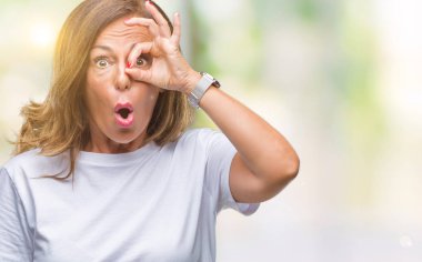 Orta yaş ok jest yapıyor izole arka plan üzerine İspanyol kadın kıdemli sürpriz yüz, göz parmaklarının arasından seyir ile şok. İmansız ifade.