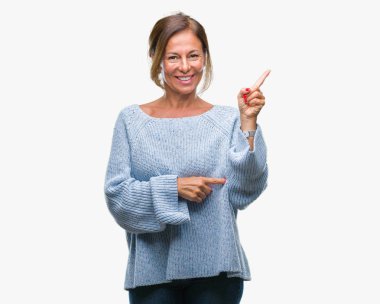 Kameraya bakarak yan el ve parmak ile işaret orta yaş üst düzey İspanyol kadın yüzünde kocaman bir gülümseme ile izole arka plan üzerinde kış kazak giyiyor.