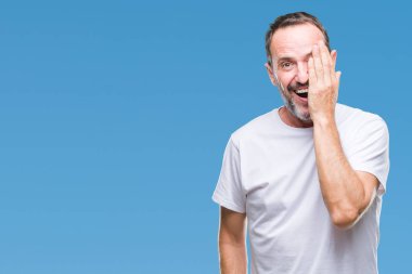 Orta yaş ağarmış komuta sizde bir göz ile yüz ve sürpriz duygu kendinden emin gülümseme ile el kapsayan izole arka plan üzerinde beyaz t-shirt giyen.