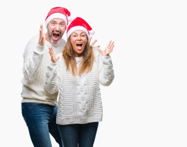 Orta yaş İspanyol çift üzerinde Noel şapka deli kutluyor arka plan izole ve başarı için kaldırdı kollarını açarak hayret ve heyecanlı çığlık gözleri açık. Kazanan kavramı