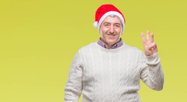 Üst düzey yakışıklı Noel şapka üzerinde gösterilen arka plan izole ve parmakları ile işaret kendinden emin ve mutlu gülümseyerek iken üçüncü.