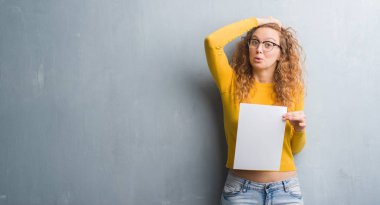 Genç Kızıl saçlı kadının kafasına, el ile vurguladı boş kağıt sayfası tutan gri grunge duvarın üzerinden şok utanç ve sürpriz suratla, öfkeli ve sinirli. Korku ve hata için üzgün.