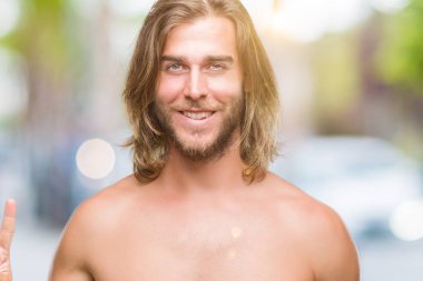 Genç yakışıklı gömleksiz adam uzun saçlı seksi vücut gösterilen ve parmakları ile işaret izole arka plan üzerinde gösterilen ikincisi ise kendinden emin ve mutlu gülümseyerek.