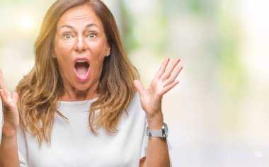 Orta yaş üst düzey İspanyol kadın deli kutluyor arka plan izole ve başarı için kaldırdı kollarını açarak hayrete ve heyecanlı çığlık gözleri açık. Kazanan kavramı