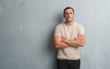 Gri grunge duvar şüpheci ve sinir, onaylamayan ifade yüz çapraz kolları olan genç beyaz adam. Negatif kişi.