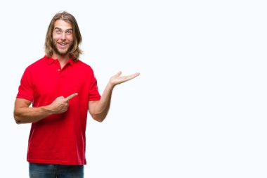 Hayret ve el ile sunulması ve parmak ile işaret ederken kameraya gülümseyen izole arka plan üzerinde uzun saçlı yakışıklı delikanlı.