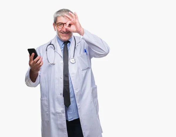 英俊的资深医生发短信发送消息使用智能手机在孤立的背景与快乐的脸微笑做确定的标志 用眼睛看着手指 — 图库照片