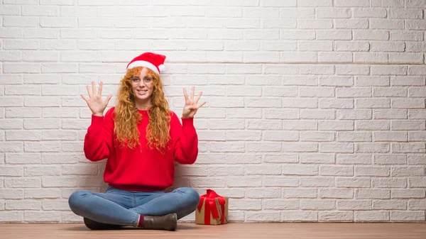 Young Redhead Woman Sitting Brick Wall Wearing Christmas Hat Showing — Stock Photo, Image