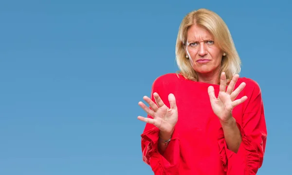 Middle age blonde woman over isolated background disgusted expression, displeased and fearful doing disgust face because aversion reaction. With hands raised. Annoying concept.