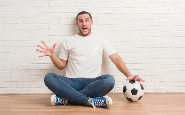 Junger Kaukasischer Mann Sitzt Über Weißer Ziegelwand Und Hält Fußballball — Stockfoto